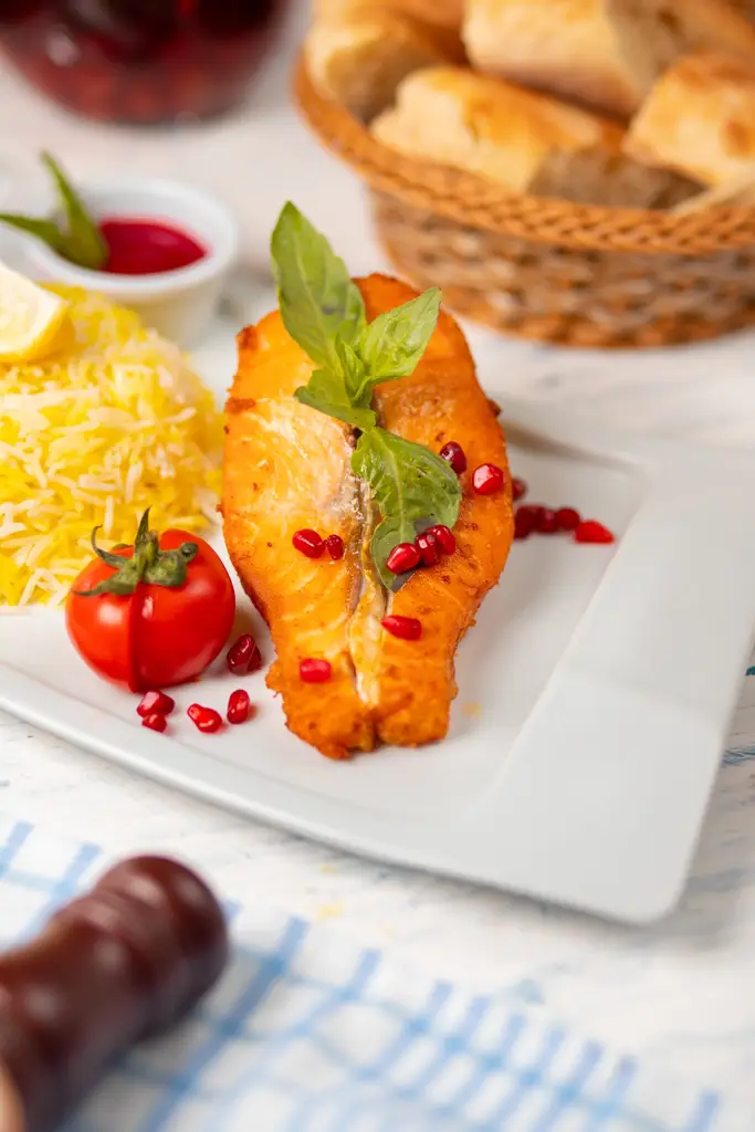 Grilled salmon fillet served with rice, tomato, pomegranate, and basil on a white plate